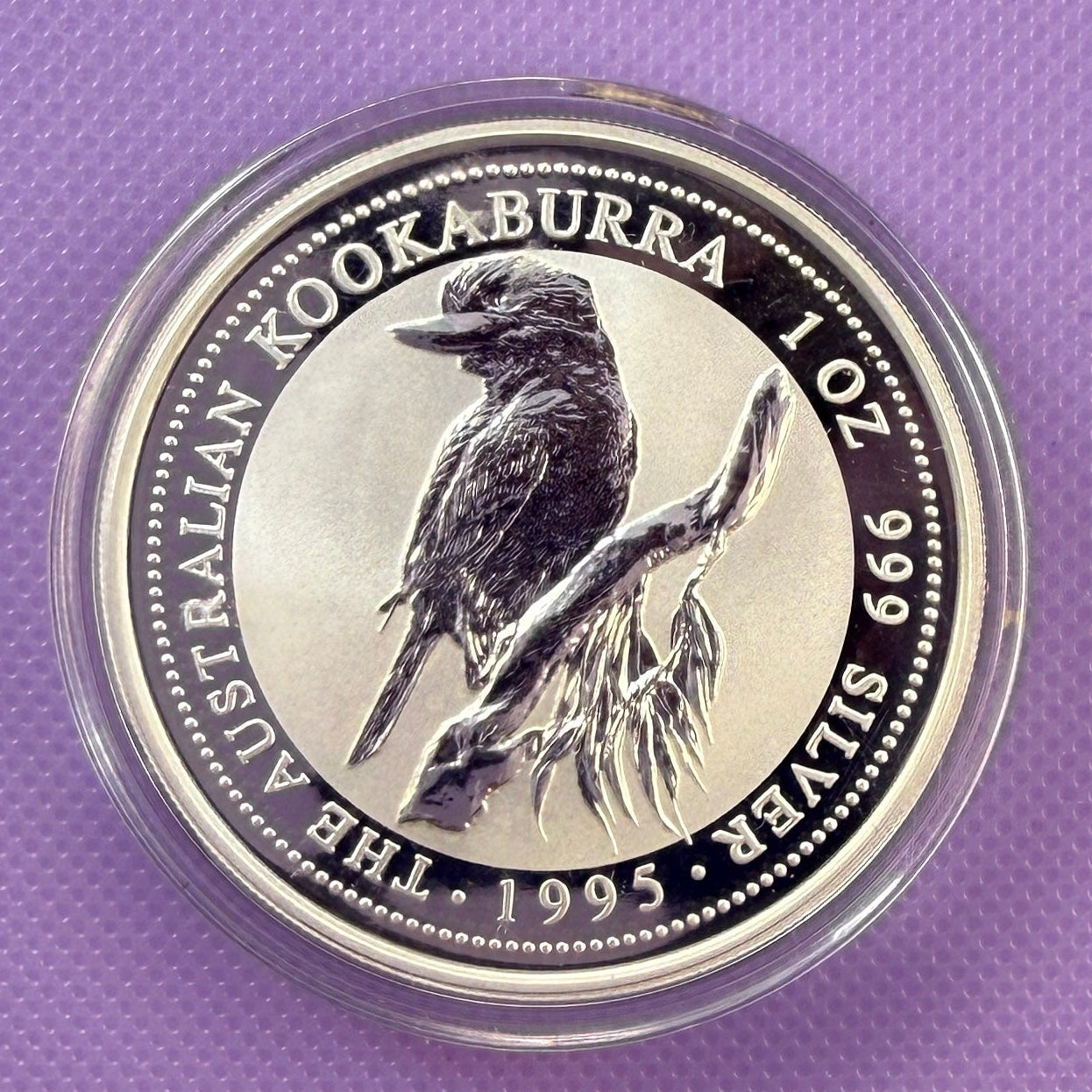 A round silver coin featuring a detailed engraving of a Kookaburra perched on a branch, with the text 'AUSTRALIAN KOOKABURRA 102 999 999 SILVER 1995' around the edge, displayed on a textured purple background.